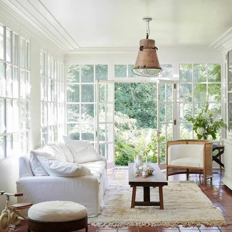 Bright living room with white furniture, wooden coffee table, and large windows.